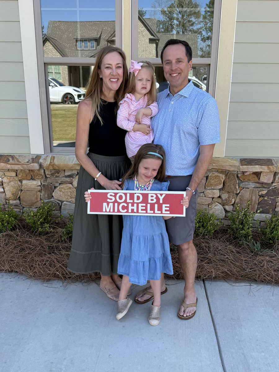 Michelle’s clients, a family with two children, holding a Sold by Michelle sign outside their home