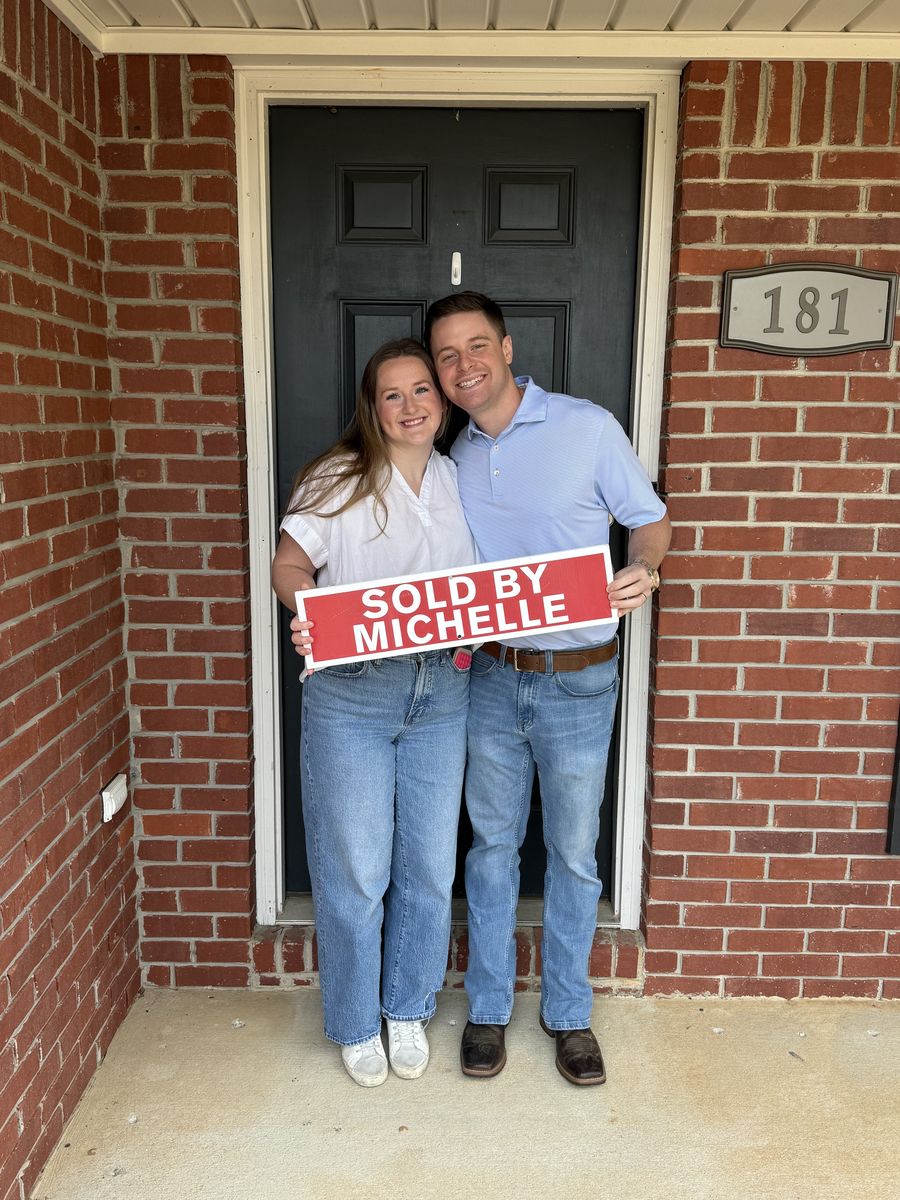 Michelle’s clients holding a Sold by Michelle sign outside a brick home